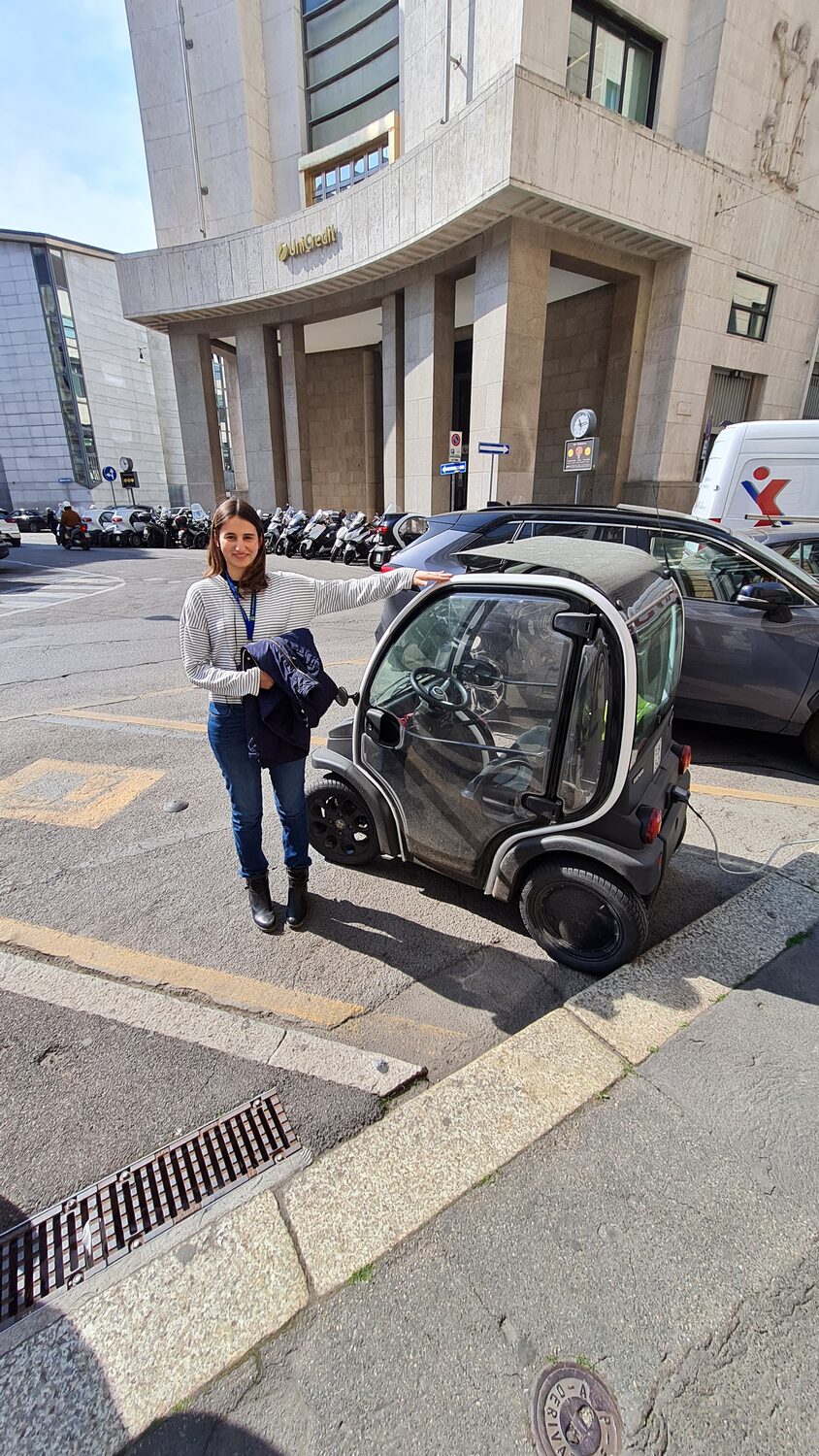 Maritza beside a tiny electric car